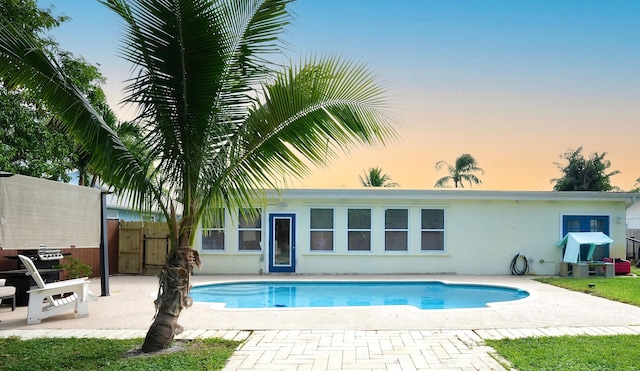 pool at dusk with a patio and fence