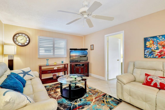 living room featuring ceiling fan, wood walls, light tile patterned floors, and a textured ceiling