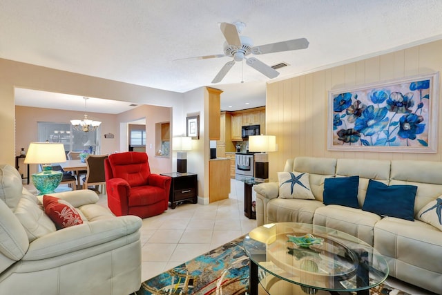 living room with light tile patterned floors, ceiling fan with notable chandelier, a textured ceiling, and wood walls