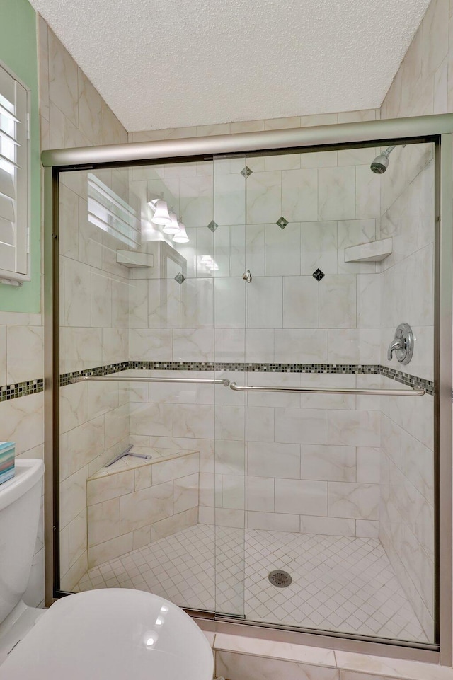 bathroom featuring a textured ceiling, toilet, and an enclosed shower