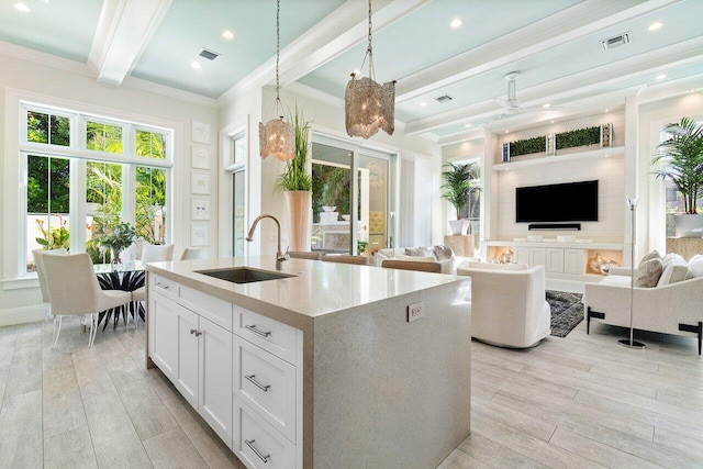 kitchen featuring white cabinetry, light wood-type flooring, hanging light fixtures, and sink