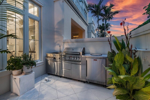 patio terrace at dusk with area for grilling and an outdoor kitchen