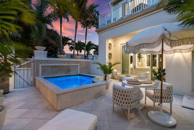 pool at dusk featuring an in ground hot tub and a patio area