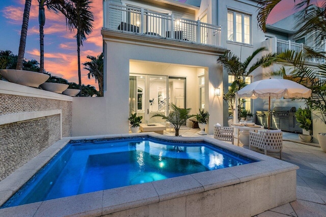 back house at dusk with an outdoor kitchen, a patio, and a balcony