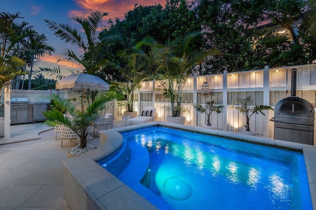 pool at dusk featuring grilling area and a patio area