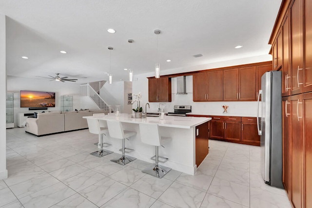 kitchen featuring wall chimney exhaust hood, hanging light fixtures, stainless steel appliances, a breakfast bar area, and a center island with sink