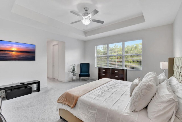 carpeted bedroom with a raised ceiling and ceiling fan