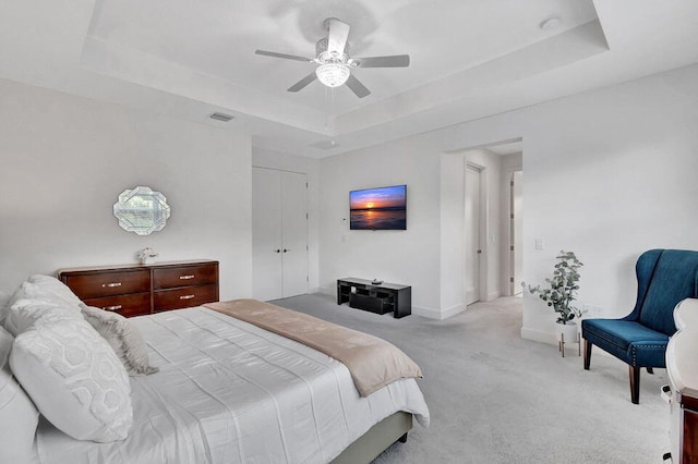 bedroom with ceiling fan, a raised ceiling, light colored carpet, and a closet