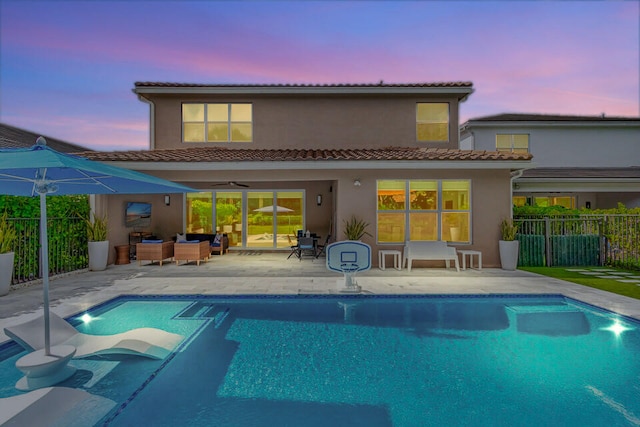 back house at dusk with outdoor lounge area, ceiling fan, a fenced in pool, and a patio