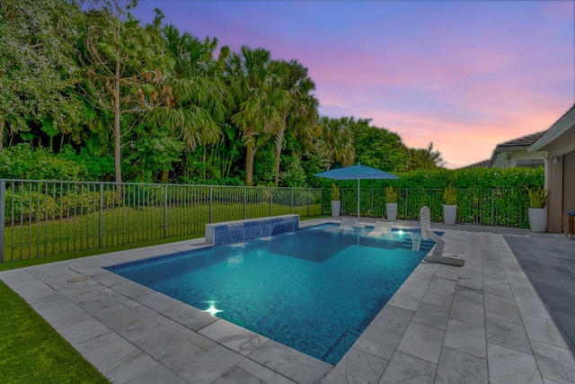 pool at dusk featuring pool water feature and a patio area