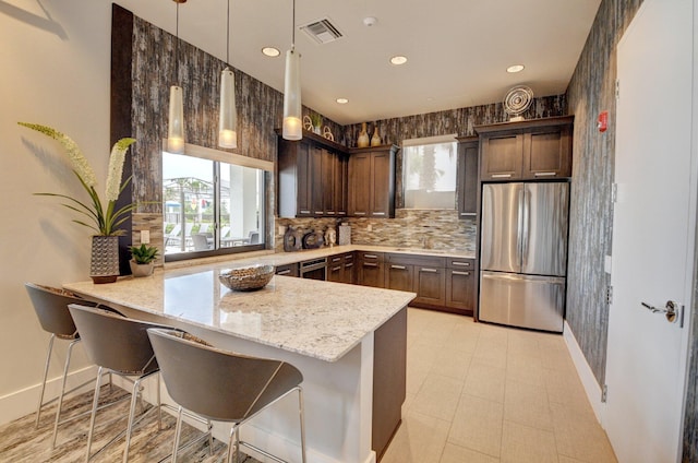 kitchen with stainless steel fridge, light stone counters, a healthy amount of sunlight, and kitchen peninsula