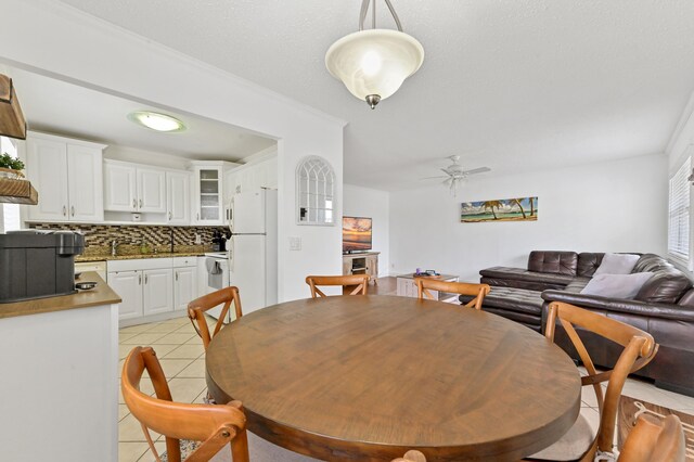 dining area featuring ceiling fan, crown molding, sink, and light tile patterned floors