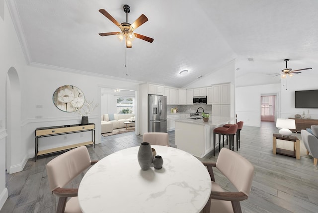 unfurnished living room featuring ceiling fan with notable chandelier, sink, crown molding, vaulted ceiling, and light wood-type flooring