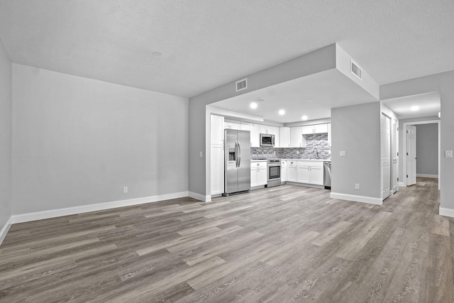 unfurnished living room featuring light hardwood / wood-style floors, a textured ceiling, and sink