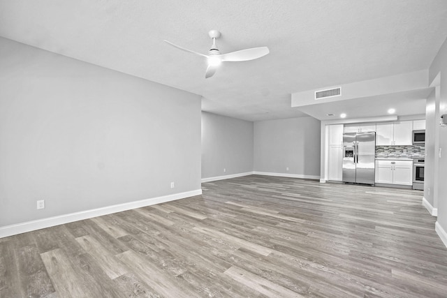 unfurnished living room featuring ceiling fan, a textured ceiling, and light wood-type flooring