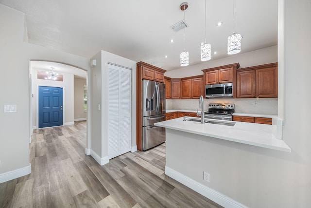 kitchen with tasteful backsplash, stainless steel appliances, decorative light fixtures, sink, and light hardwood / wood-style floors