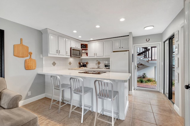 kitchen featuring white cabinetry, backsplash, kitchen peninsula, a kitchen bar, and appliances with stainless steel finishes