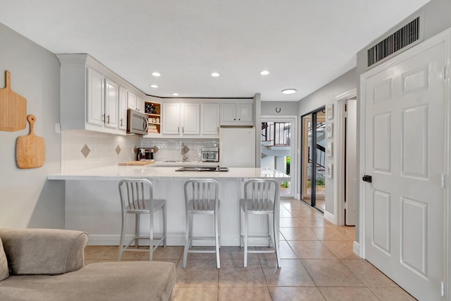 kitchen featuring white fridge, kitchen peninsula, a breakfast bar area, and white cabinetry