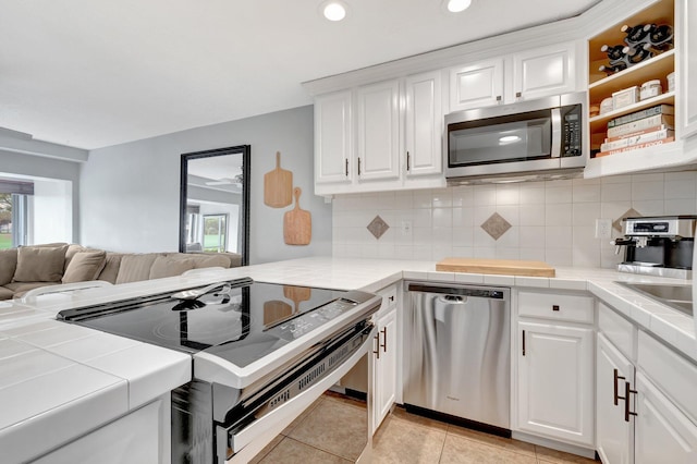 kitchen featuring tile countertops, backsplash, white cabinetry, and stainless steel appliances