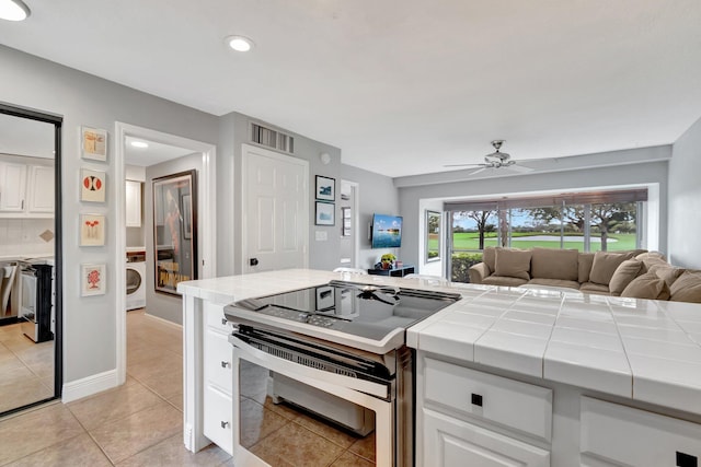 kitchen with stainless steel range, light tile patterned floors, tile countertops, and white cabinets