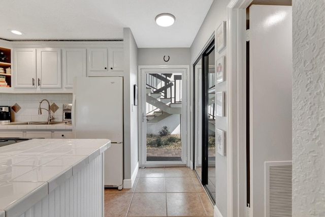 kitchen featuring tile countertops, white fridge, white cabinets, and a healthy amount of sunlight