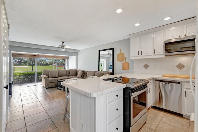 kitchen featuring stainless steel appliances, tasteful backsplash, kitchen peninsula, tile countertops, and white cabinets