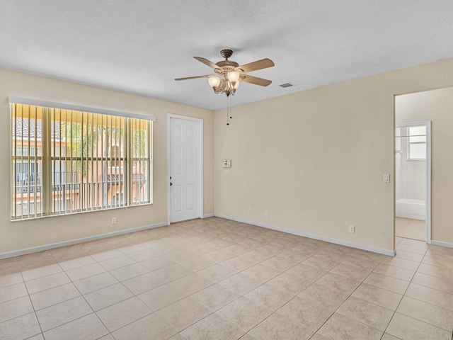 tiled empty room featuring ceiling fan, a healthy amount of sunlight, and a textured ceiling