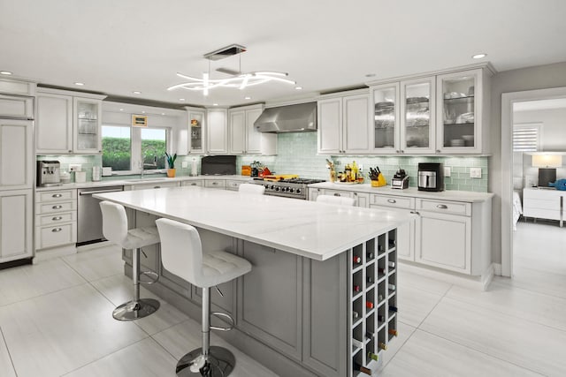 kitchen with appliances with stainless steel finishes, wall chimney exhaust hood, a center island, pendant lighting, and decorative backsplash