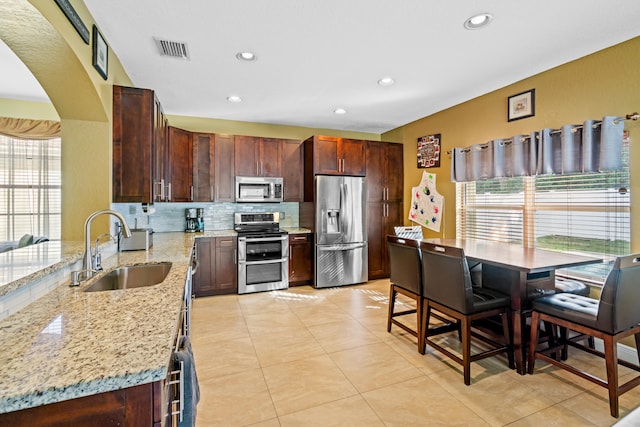 kitchen with light stone counters, decorative backsplash, sink, light tile patterned floors, and appliances with stainless steel finishes