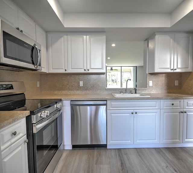 kitchen featuring white cabinetry, sink, appliances with stainless steel finishes, backsplash, and light wood-type flooring