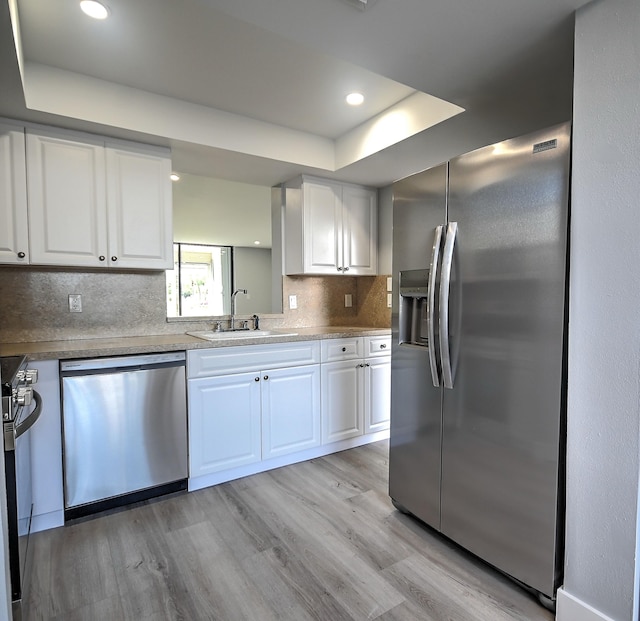 kitchen featuring light hardwood / wood-style floors, stainless steel appliances, white cabinets, sink, and a raised ceiling