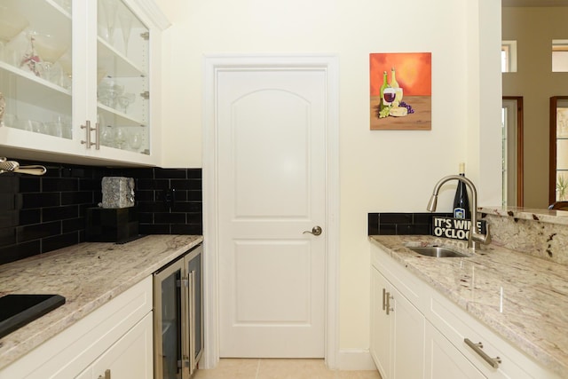 kitchen with sink, backsplash, light tile patterned flooring, white cabinets, and light stone countertops