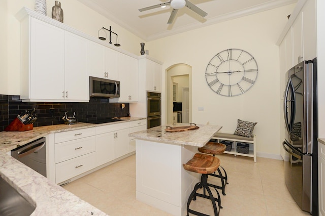 kitchen with appliances with stainless steel finishes, light stone counters, white cabinets, a center island, and light tile patterned floors