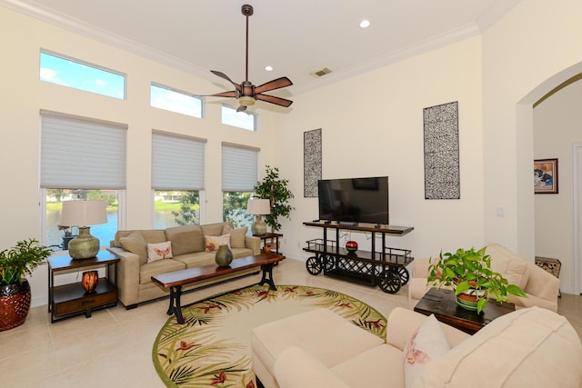 tiled living room with ceiling fan, plenty of natural light, crown molding, and a high ceiling