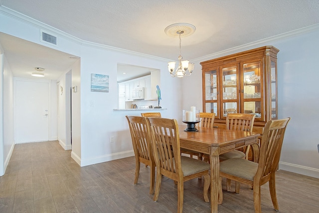 dining room with hardwood / wood-style flooring, a textured ceiling, an inviting chandelier, and ornamental molding