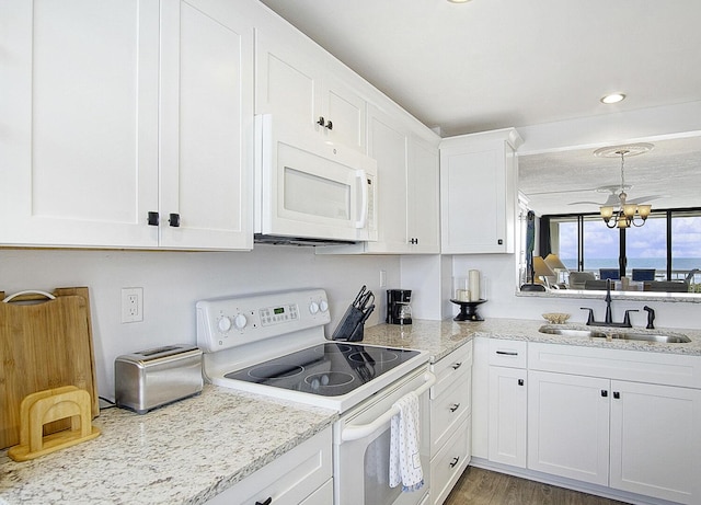 kitchen with light stone counters, an inviting chandelier, white appliances, white cabinetry, and a sink