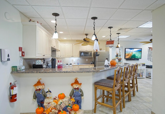 kitchen featuring stainless steel appliances, dark stone counters, kitchen peninsula, ceiling fan, and white cabinetry