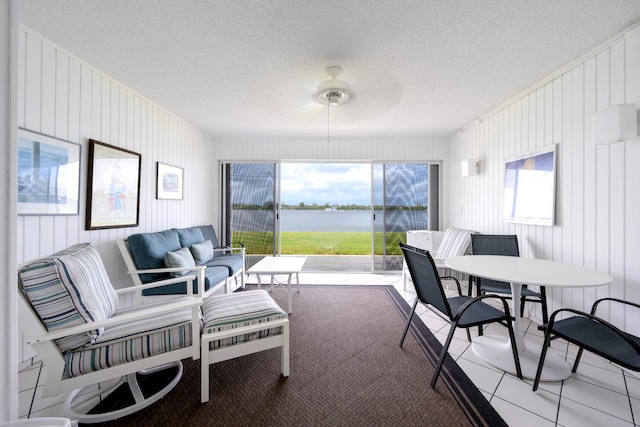 interior space with ceiling fan, a textured ceiling, wooden walls, and a water view