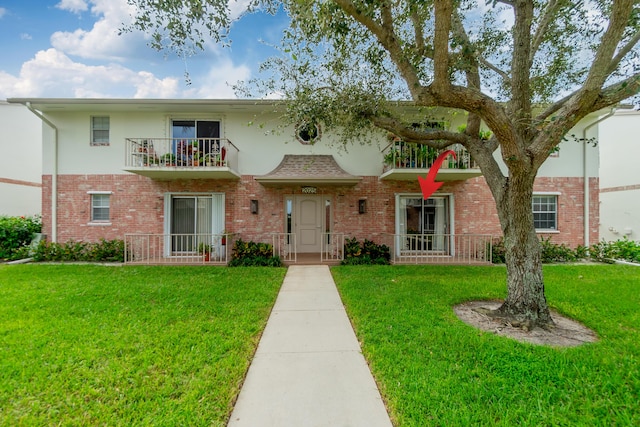 view of front of home with a front yard, brick siding, and a balcony