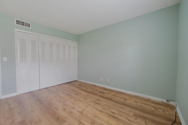 unfurnished bedroom featuring light wood finished floors, ensuite bath, visible vents, and baseboards