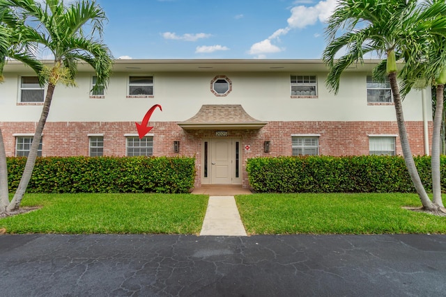 townhome / multi-family property featuring brick siding, a front lawn, and stucco siding