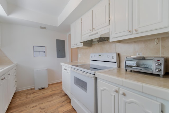 kitchen featuring white electric stove, tile countertops, under cabinet range hood, white cabinets, and electric panel