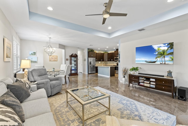 living room featuring ceiling fan with notable chandelier and a tray ceiling