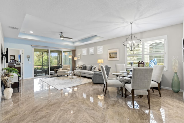 dining space with ceiling fan with notable chandelier, a textured ceiling, and a tray ceiling