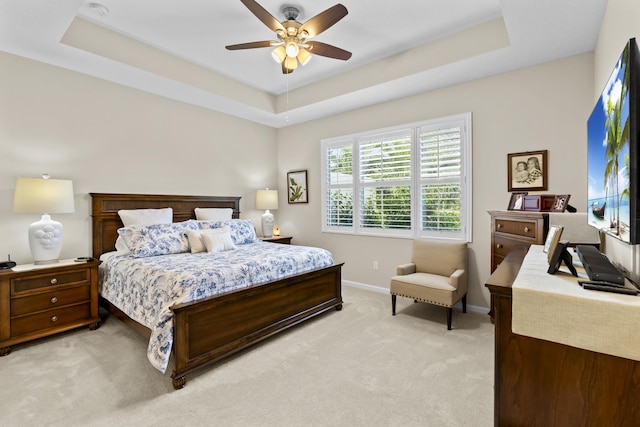 bedroom with a raised ceiling, light colored carpet, and ceiling fan