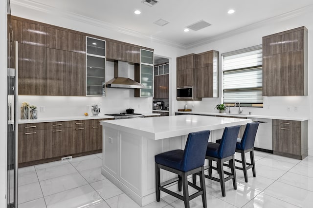 kitchen featuring a center island, wall chimney exhaust hood, stainless steel appliances, a breakfast bar, and ornamental molding