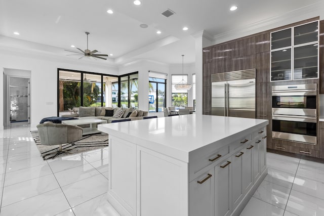 kitchen featuring crown molding, hanging light fixtures, appliances with stainless steel finishes, a tray ceiling, and a kitchen island