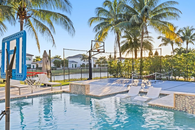 view of pool featuring pool water feature, a water view, and basketball hoop