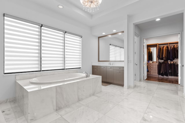 bathroom with vanity, a relaxing tiled tub, and a notable chandelier