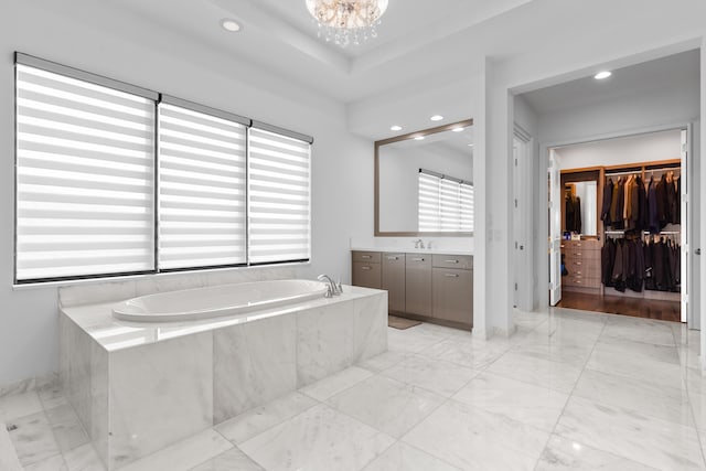 bathroom with vanity, a chandelier, and tiled tub